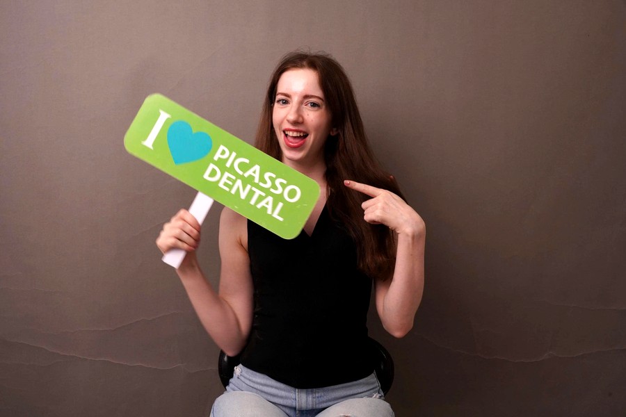 Smiling international patient holding I love Picasso Dental sign after treatment